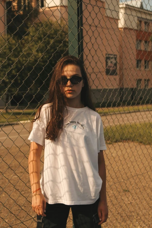 a young woman standing in front of a fence