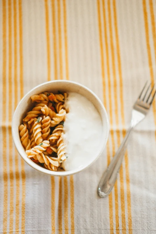 a bowl of noodles sits on a table next to a fork