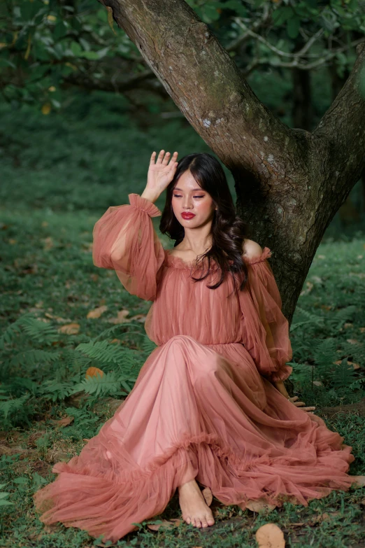 a woman in an orange dress is seated under a tree