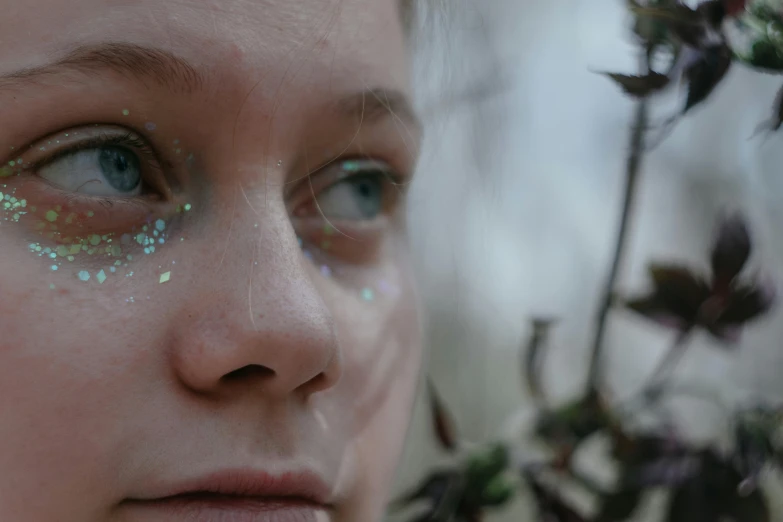 a woman with glitter on her face next to flowers