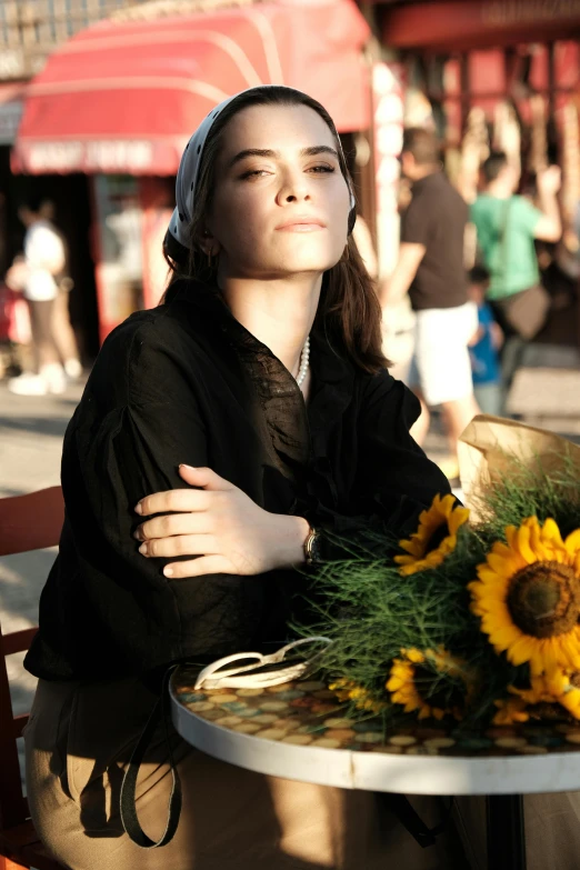 a woman is smiling while leaning on the table with a sunflower