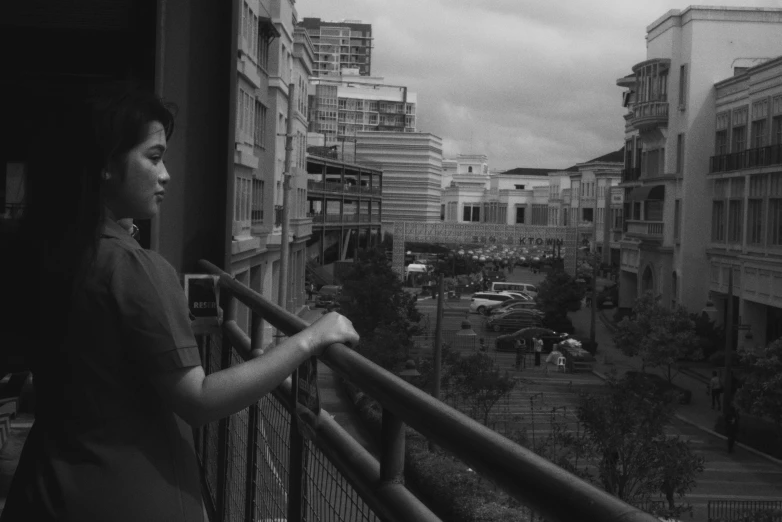 a woman standing on the balcony of her apartment looking out into a street full of buildings