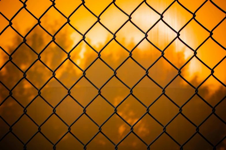 a chain link fence with the setting sun in the distance