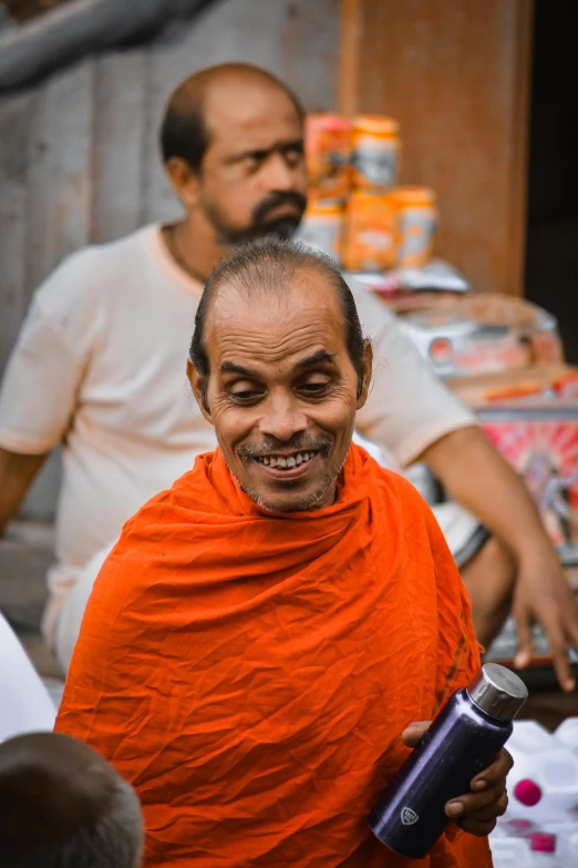 man in orange robes with beard holds up a can