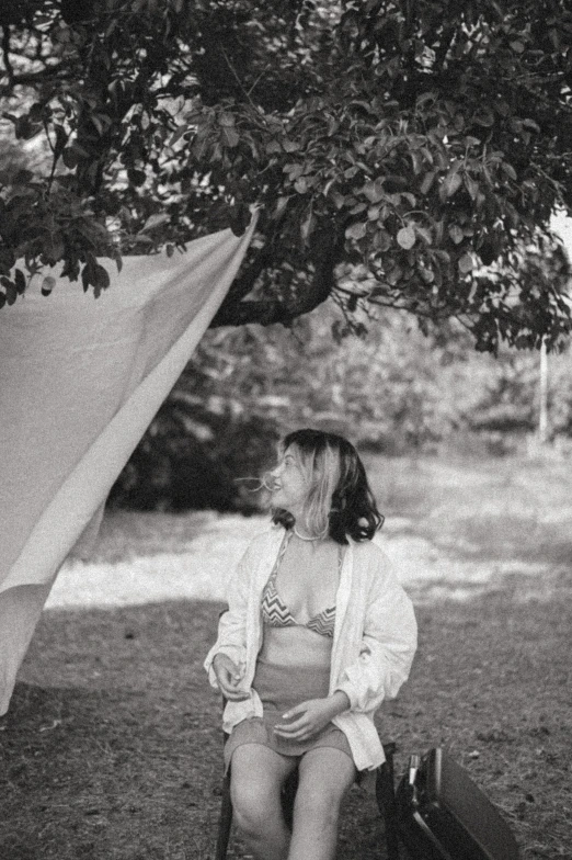 a woman is sitting under a tree while talking on her cell phone