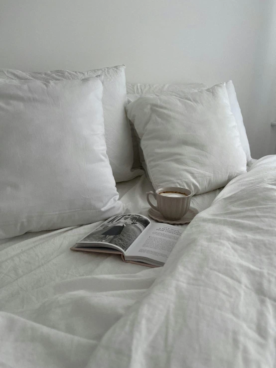 a cup of coffee sits on a white blanket as it rests next to a stack of pillows