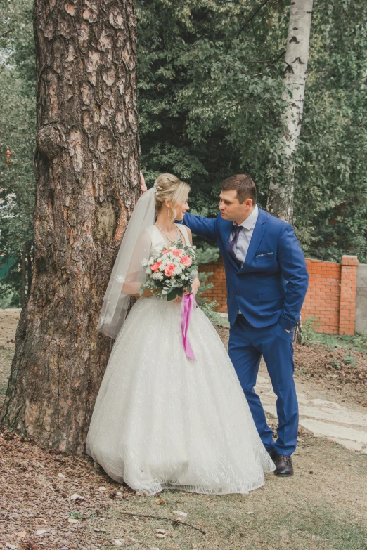 bride and groom in wedding dress standing next to a tree