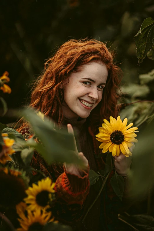 the woman smiles holding a large sunflower