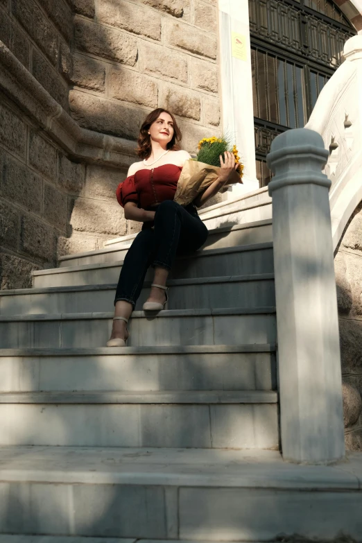 a woman sits on steps with a basket and flower bouquet