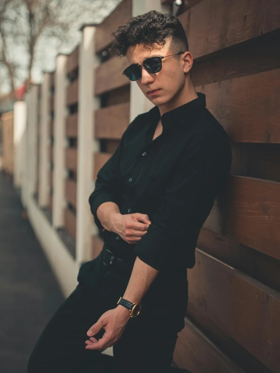 a man wearing a pair of sunglasses leaning on a wooden wall