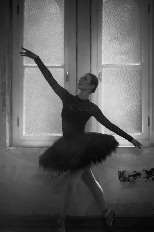 a ballerina is wearing black ballet dress and posing in front of window