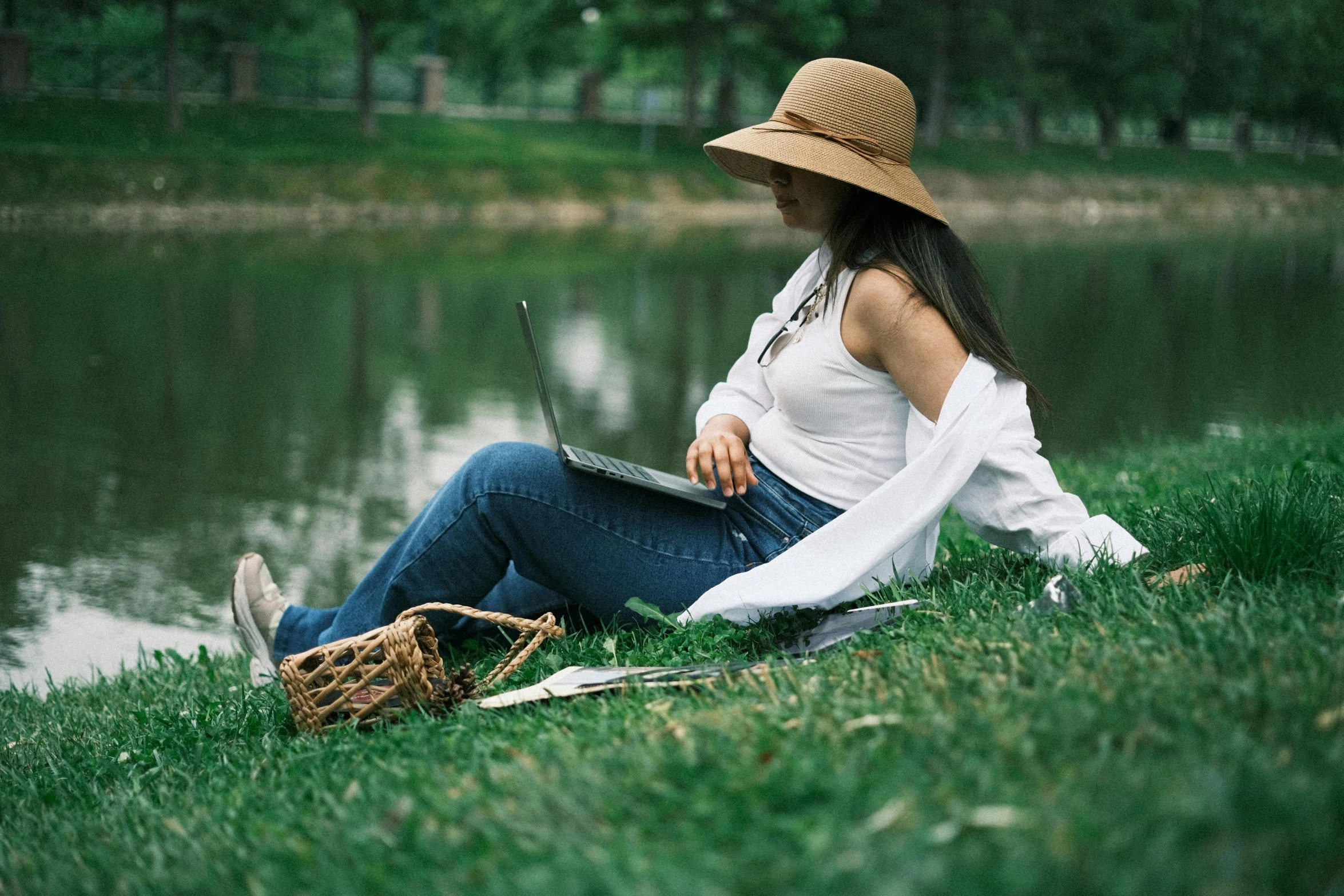 a woman sits on the grass while using her laptop