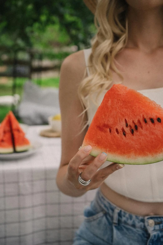 woman holding watermelon slice with fingers in mouth