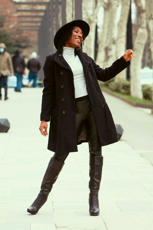 a woman is standing and wearing boots and a coat