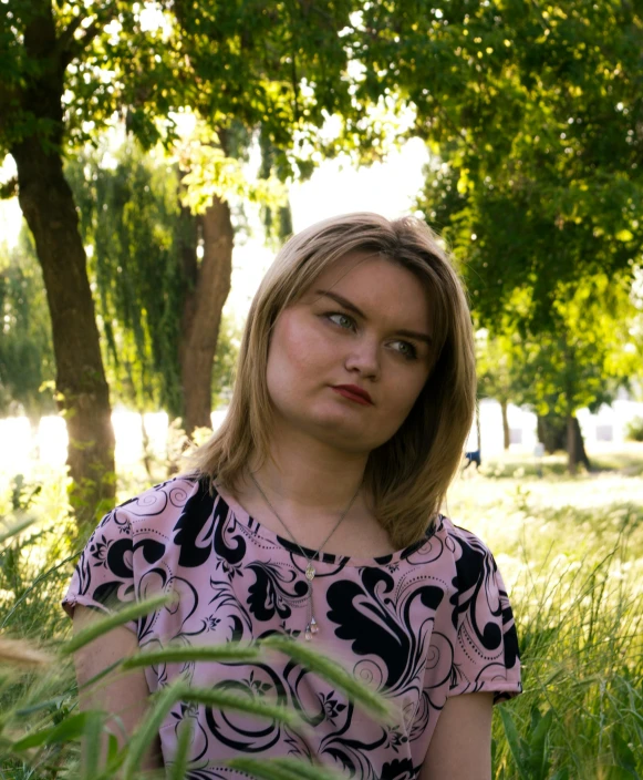 a  sitting in grass in front of trees