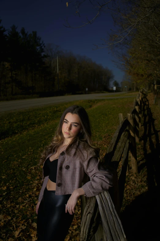 a girl leaning against a wooden rail in a field