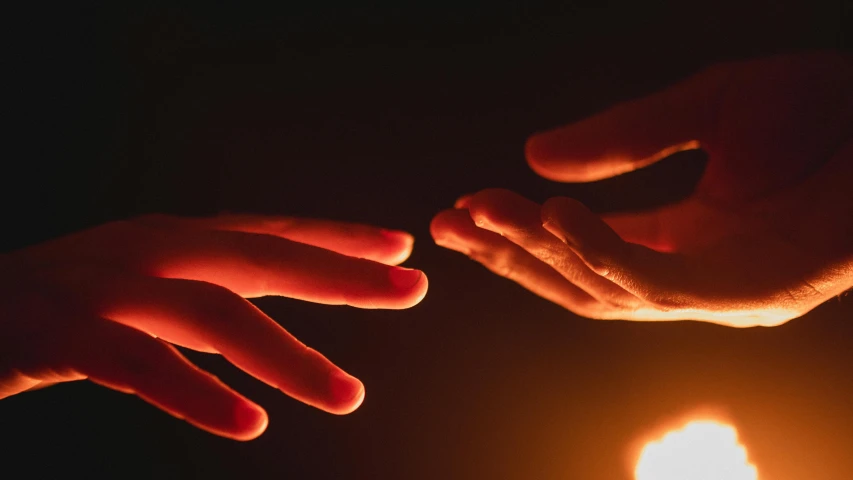 two hands reaching toward each other over a lit candle