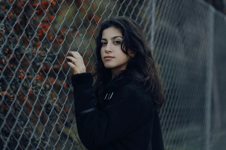 a woman is leaning against a fence holding onto soing