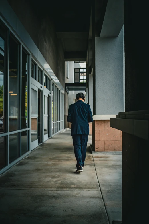 man in dark clothing walking down walkway next to windows