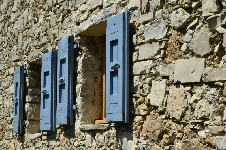 a stone house with blue windows and closed shutters