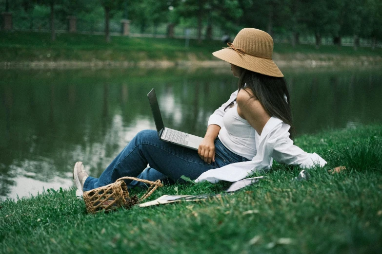 girl wearing hat sitting on grass looking at a laptop