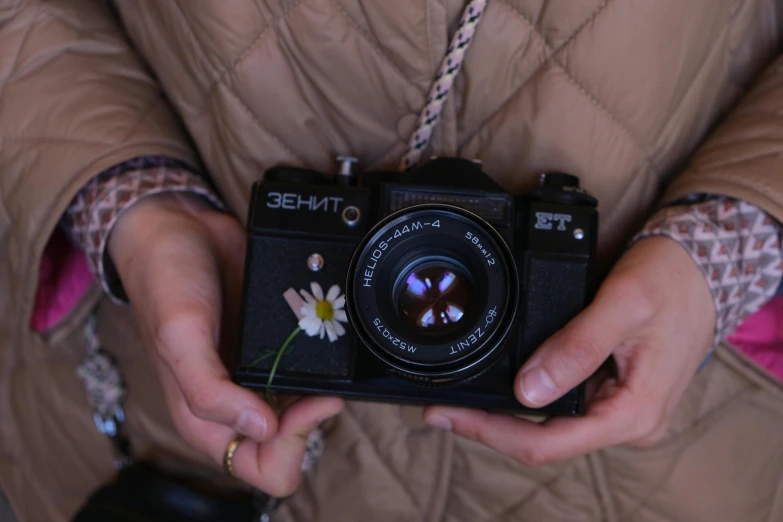 woman in a brown jacket holds a camera