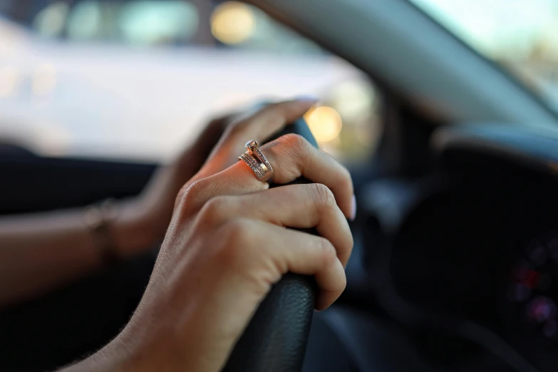 a hand in the steering wheel holds on to a yellow diamond ring