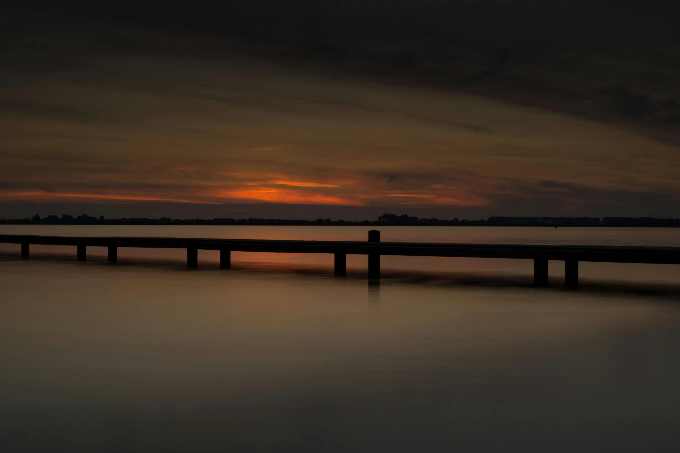 there is a dark long wooden pier at sunset