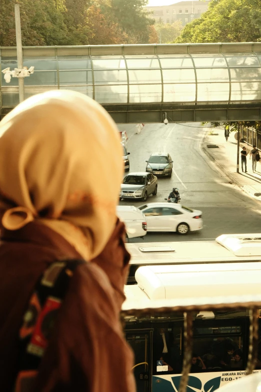 a woman with a headscarf stands on a balcony looking down at cars