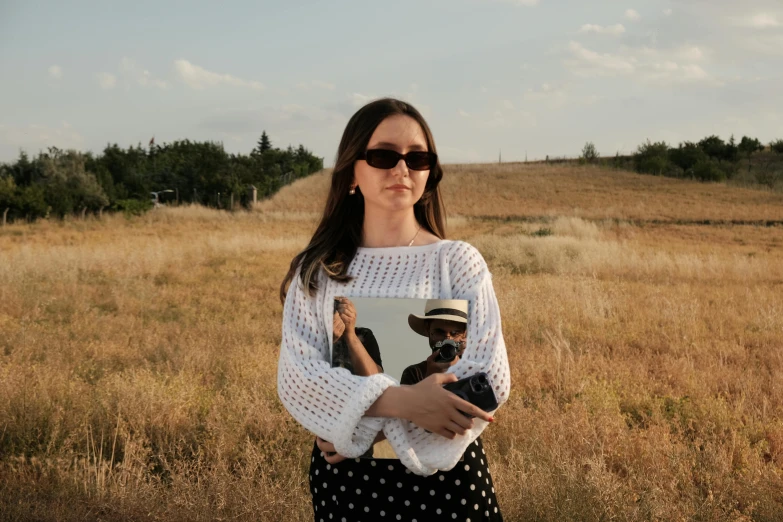 a woman wearing shades and a sweater holding an object in her hand