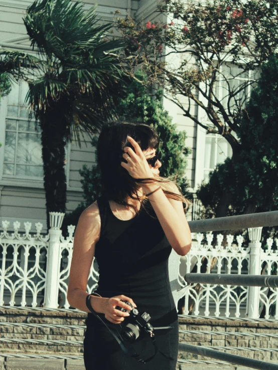 a woman wearing a black dress standing with a camera around her neck