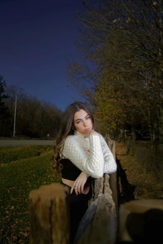 a woman leans against a fence looking at the camera