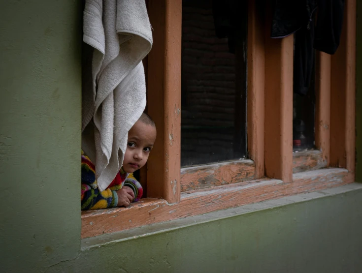 a little boy looks out of a window with a towel hanging up