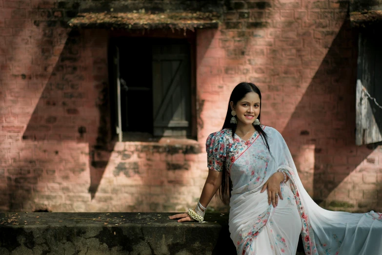 a woman with long hair and wearing a sari standing in front of a brick building