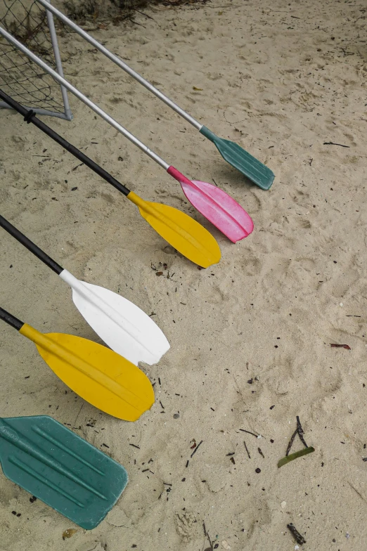 four paddles sitting on a sandy surface next to poles