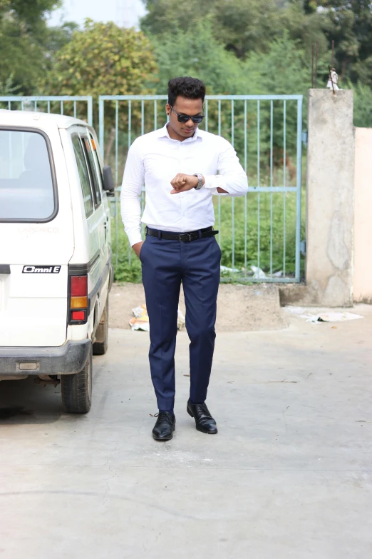 a man in a white shirt and blue pants walking near his car