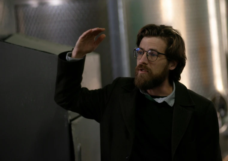 a man wearing glasses standing next to a metal tank