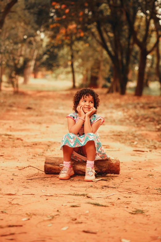 the little girl is sitting on a piece of wood