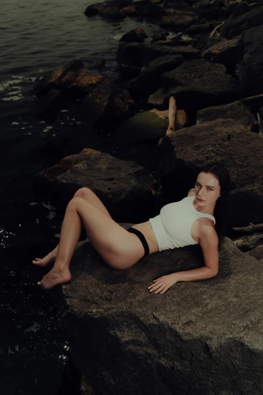 a woman in a swimsuit lies on a rock by the water