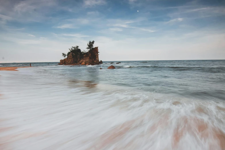 the ocean waves come in and near a rock with two trees