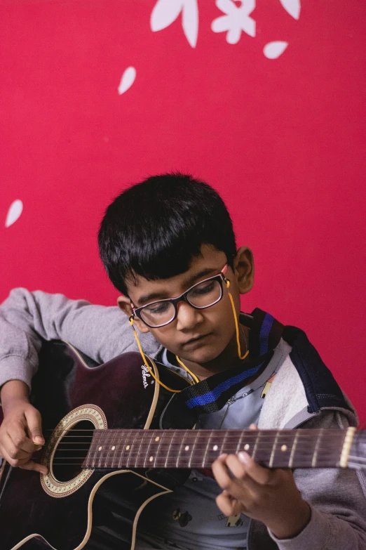 a boy playing guitar against red backdrop
