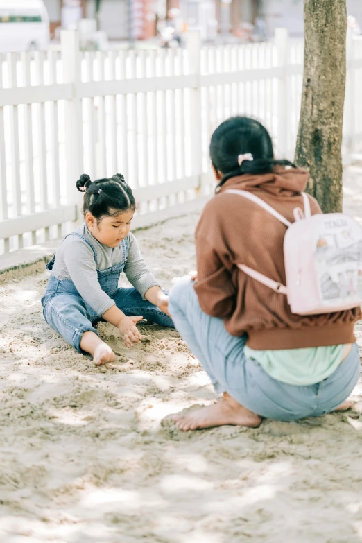 two girls sit in the sand playing with sand at a park