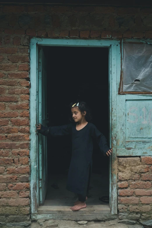 young indian girl standing in doorway with arms outstretched in dark alleyway