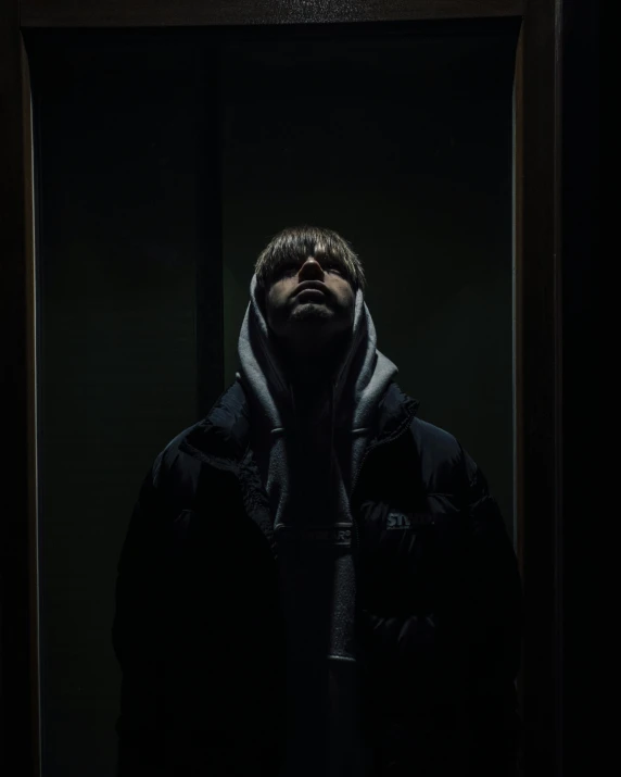 man in dark with hooded up holding his face