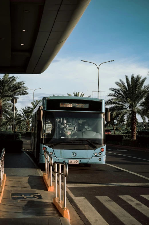 there is a light blue city bus stopped at the bus stop