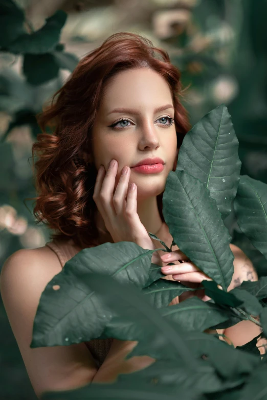 a woman with long red hair posing behind leaves