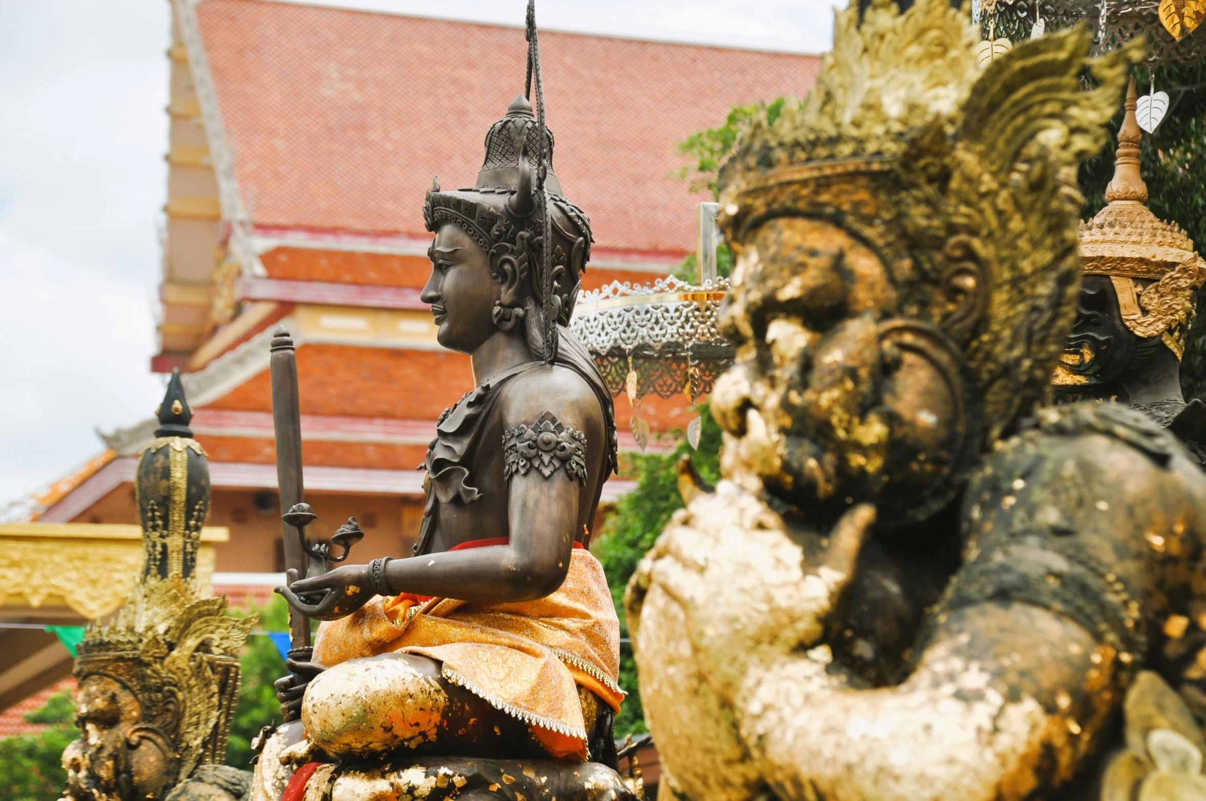 statues in the shape of indian gods with red tile buildings behind them