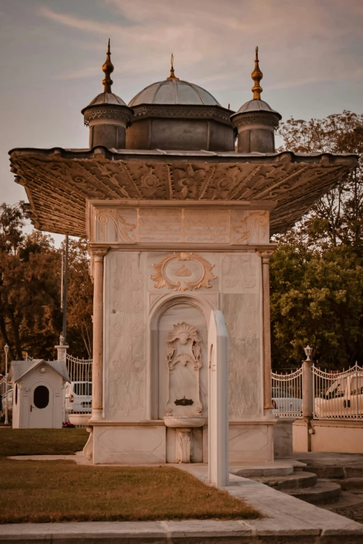 a small fountain and pavilion is near a tree