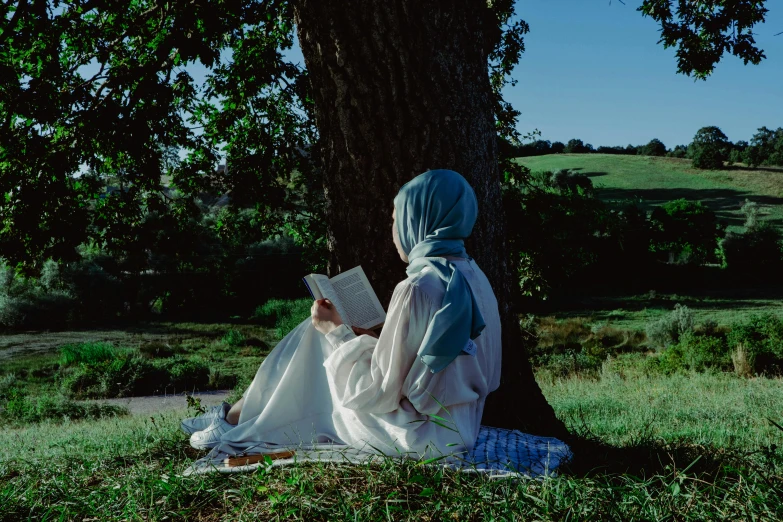 there is a woman sitting under a tree reading a book