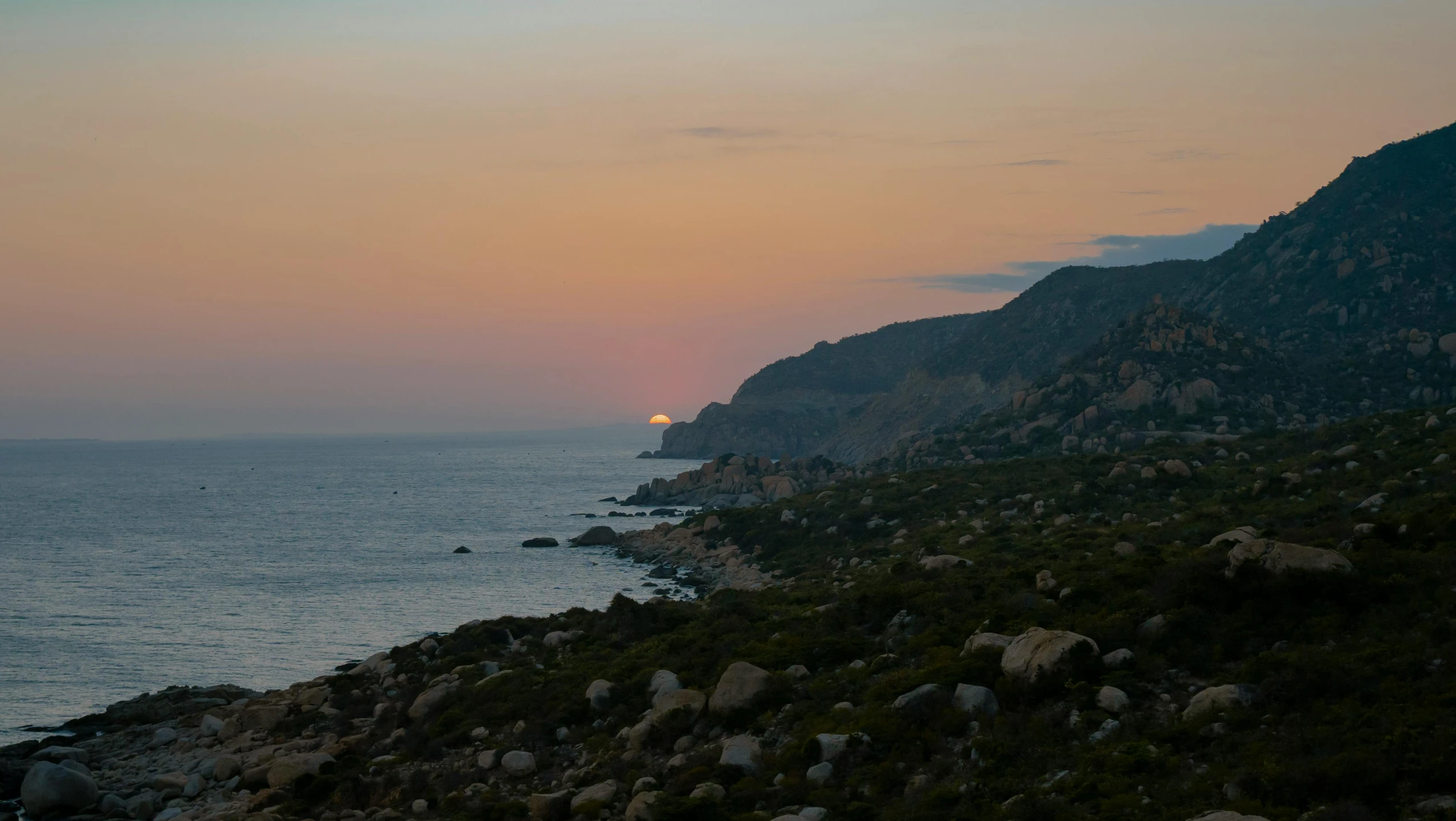 the sun is setting on the ocean along with some mountain